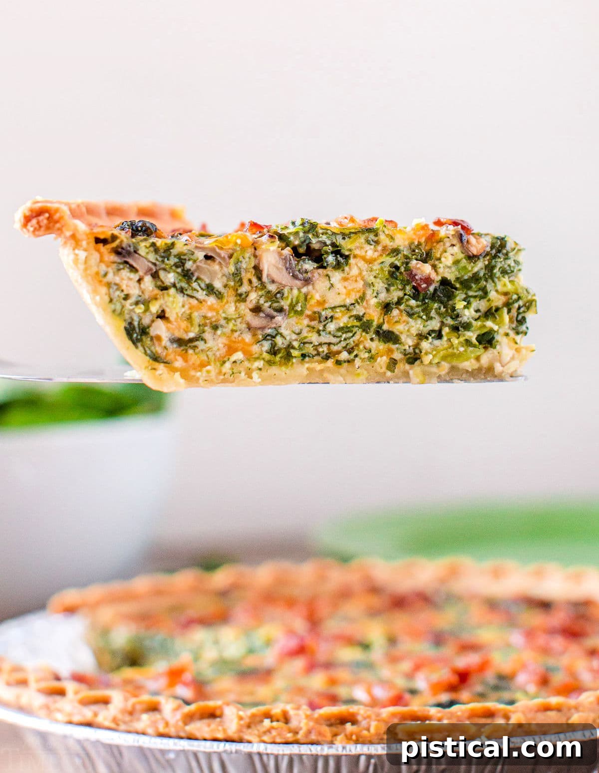 A delicious slice of Spinach Mushroom Quiche being lifted from the pie plate, showing its thick, creamy filling.