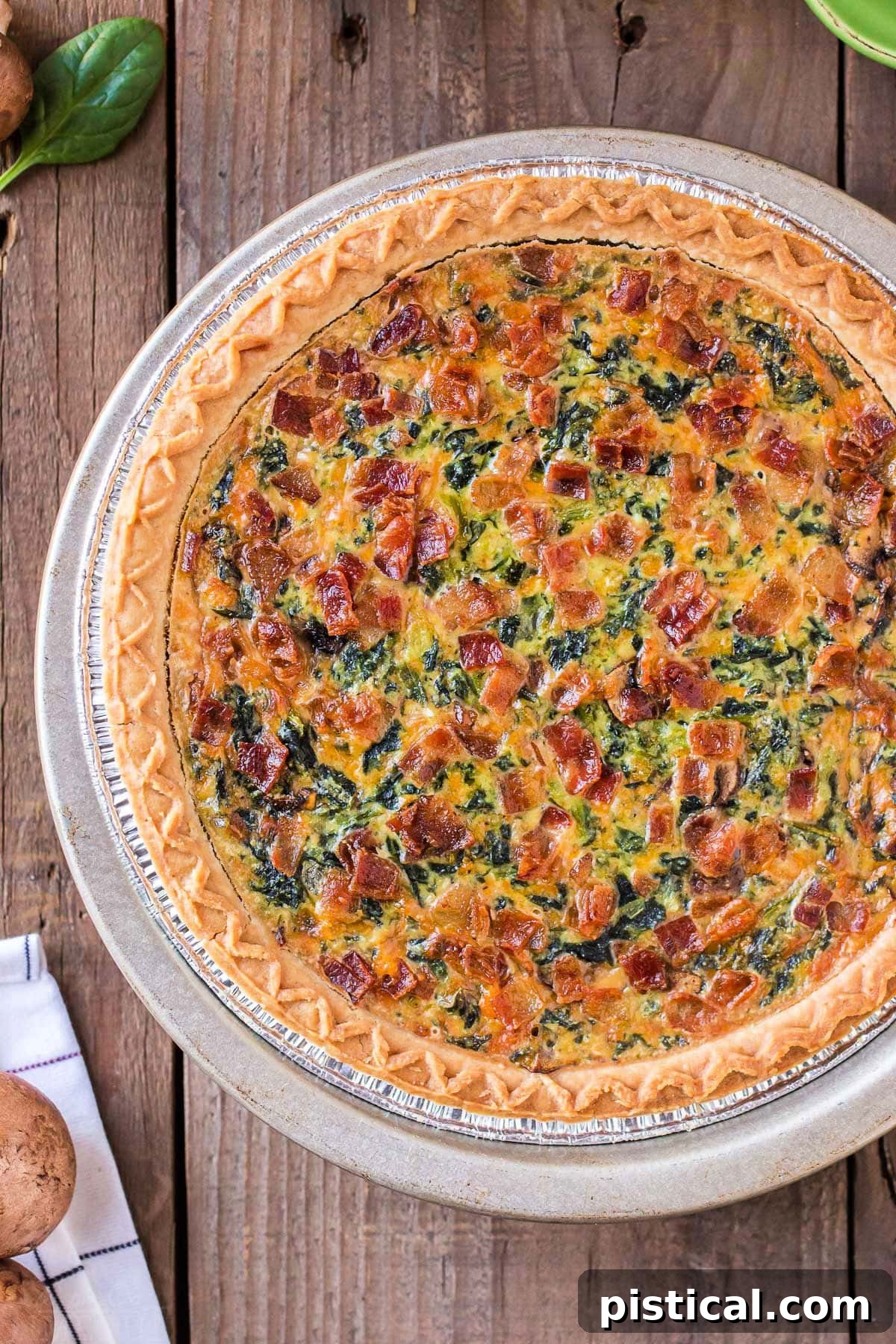 A top-down view of a perfectly baked, whole Spinach Quiche resting on a wooden surface, ready to be enjoyed.
