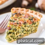 A close-up of a slice of spinach quiche on a white plate, showcasing the rich filling.
