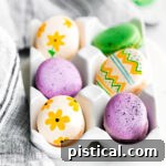 french macarons decorated as easter eggs sitting in white egg crate.