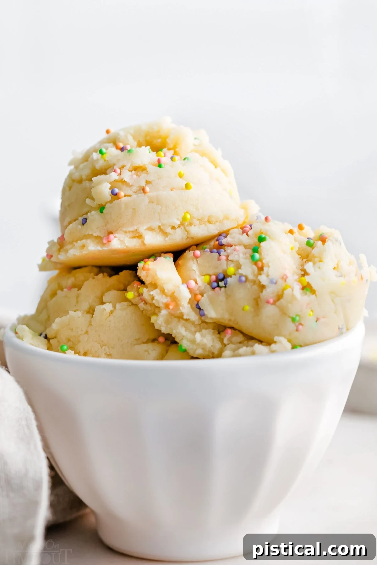 Ready-to-Eat Sugar Cookie Dough 4 Three scoops of edible cookie dough, generously topped with sprinkles, served in a pristine white ice cream cup.