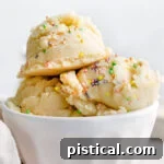 Three scoops of edible cookie dough in a white ice cream cup, generously topped with sprinkles.