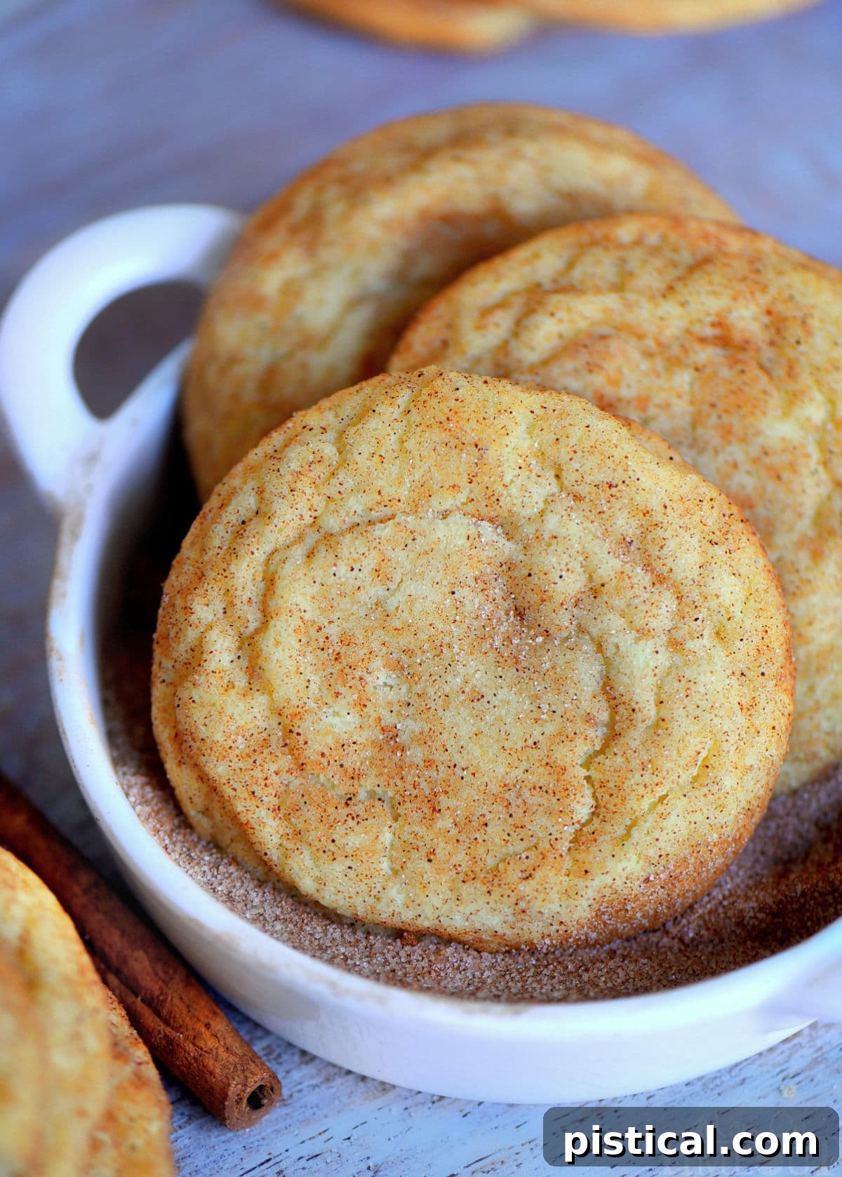Snickerdoodle cookie dough balls being rolled in a cinnamon sugar mixture in a small white bowl.