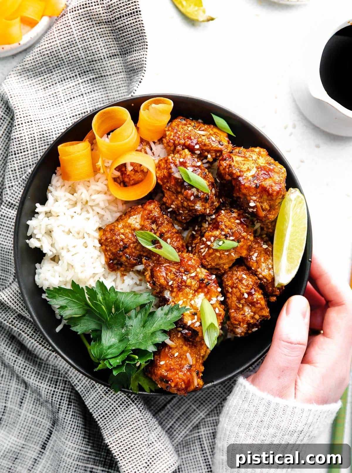 A black bowl filled with perfectly cooked teriyaki chicken and white rice, garnished with orange peels, a lime wedge, and fresh parsley for a vibrant presentation.