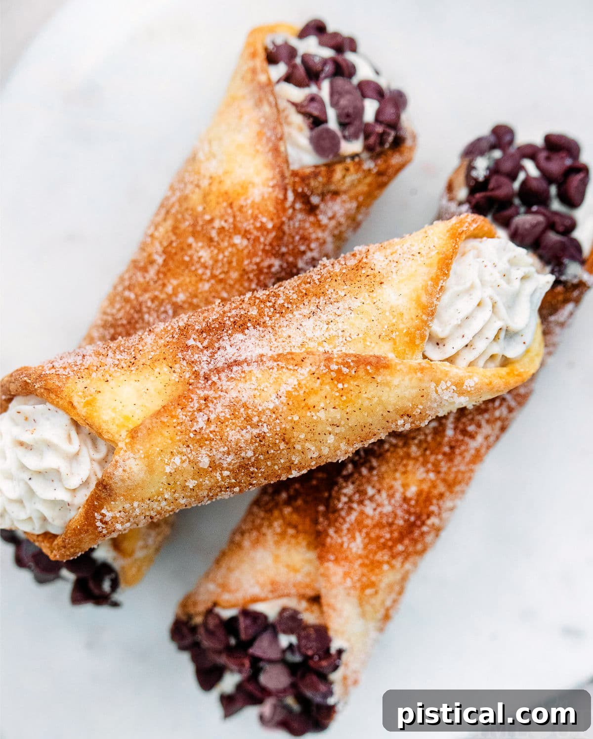 Close up look at cannolis with a churro coating. Three stacked on a white plate.