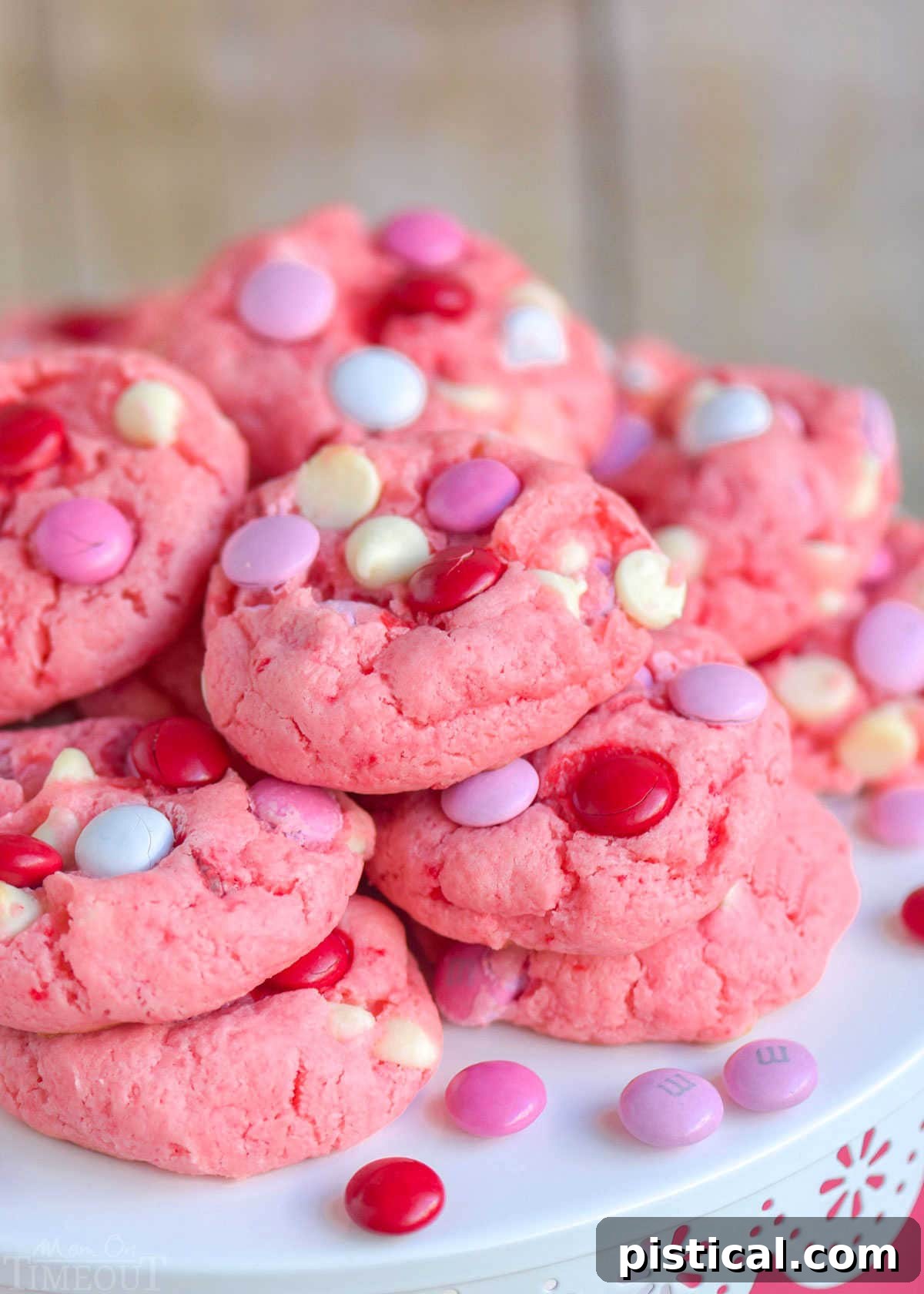 A stack of super moist Strawberry Cake Mix Cookies adorned with colorful M&Ms and white chocolate chips, elegantly presented on a white metal cake stand. Perfect for any celebration!