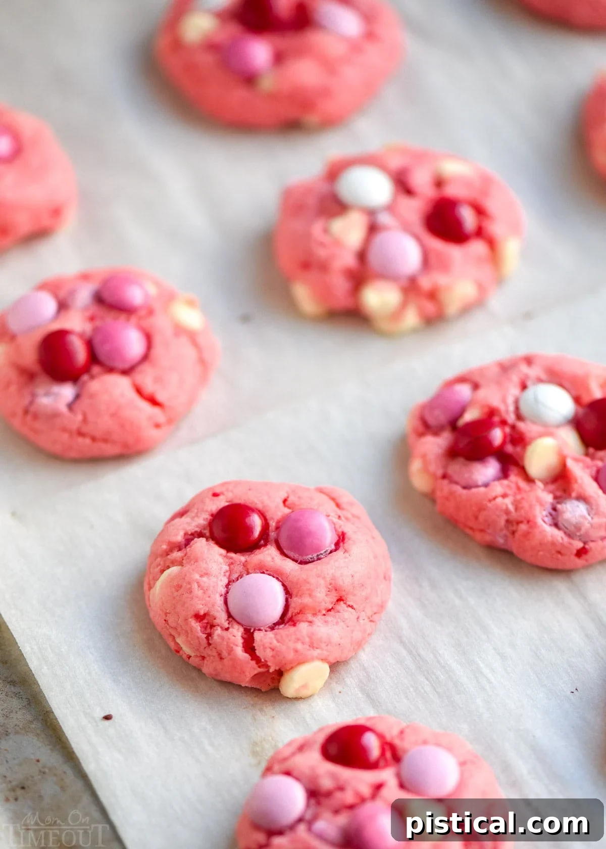 Freshly baked strawberry cake mix cookies, still warm from the oven, cooling on a parchment-lined cookie sheet. Their delicate pink color and soft centers are visible.
