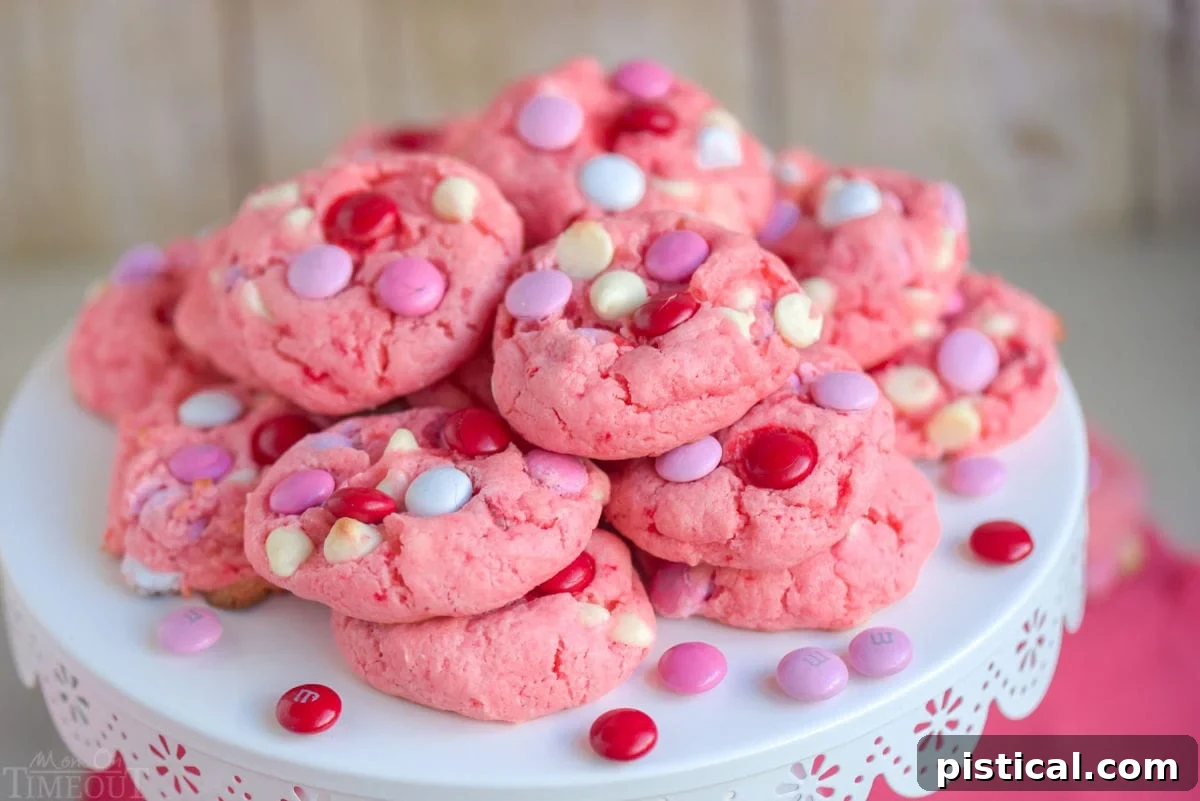 An inviting pile of freshly baked Strawberry Cake Mix Cookies, garnished with M&Ms and white chocolate chips, arranged beautifully on a white metal cake stand. A perfect dessert display.
