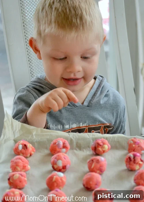 Bryce, a young boy, happily showing off a delicious Strawberry and White Chocolate Cake Mix Cookie with M&Ms, illustrating their irresistible appeal.