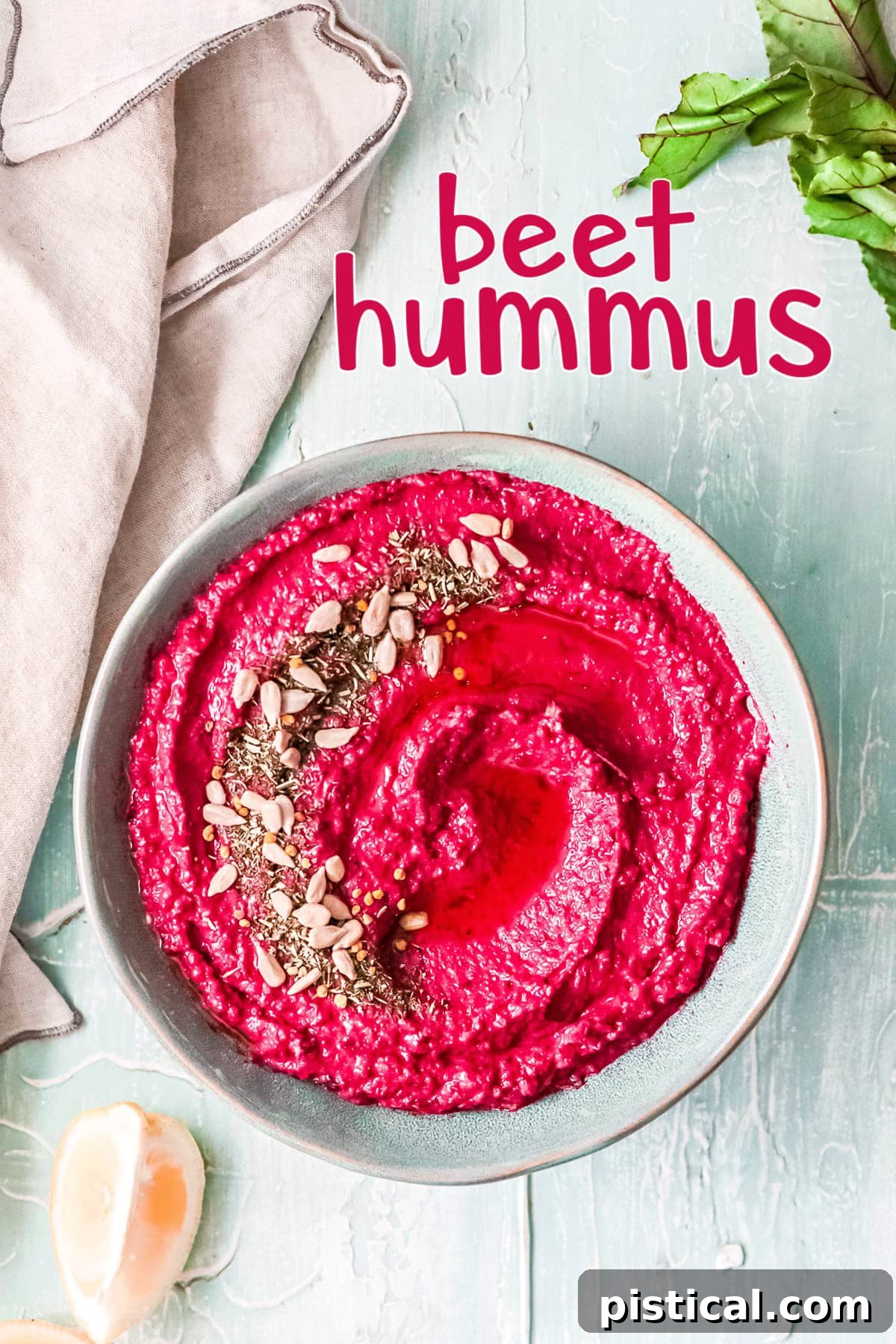 Beet Hummus: Vibrant, Versatile, Delicious 2 A vibrant bowl of roasted beet hummus, garnished with a drizzle of olive oil and a sprinkle of seeds, invitingly presented in a light blue bowl on a textured background.