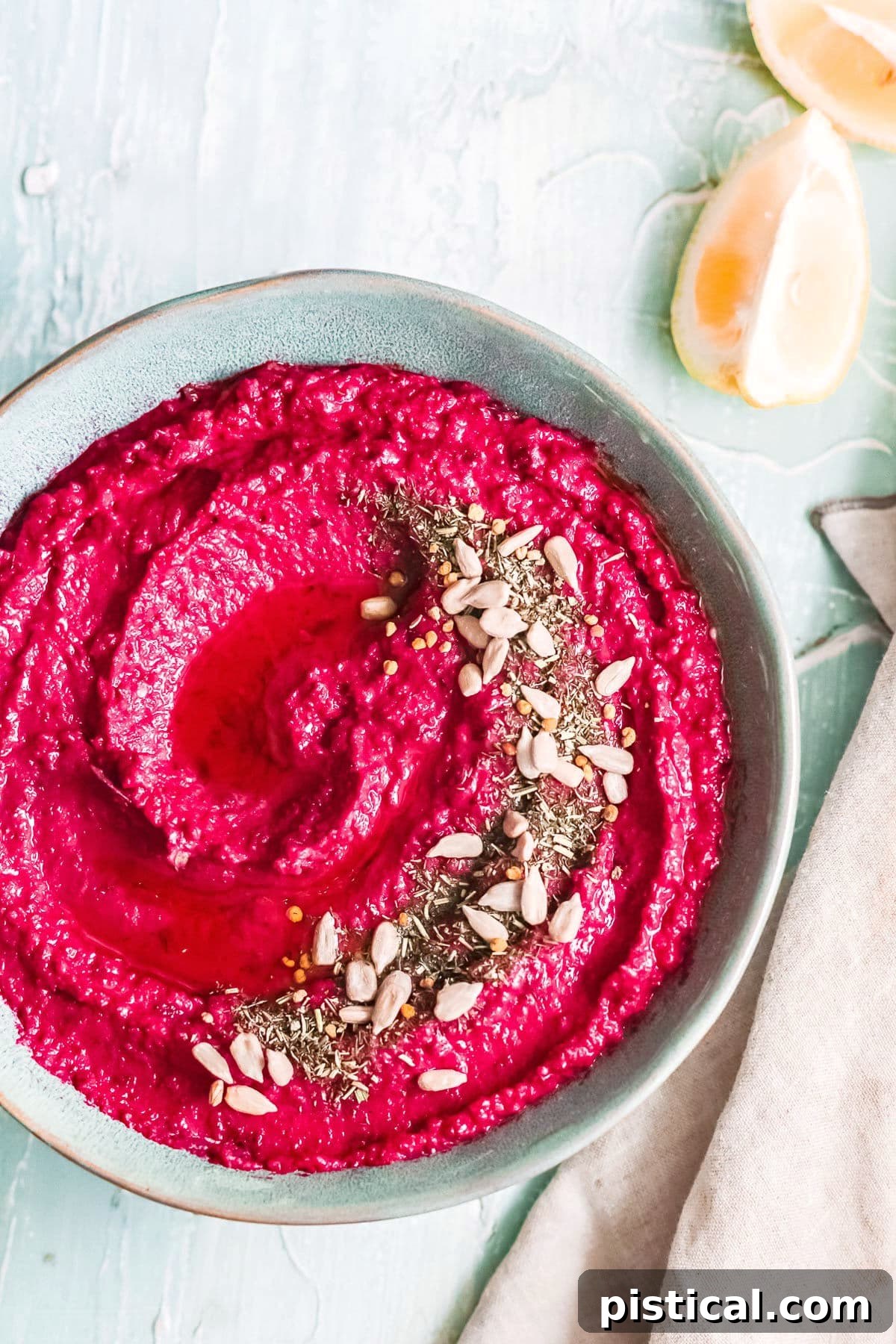 Beet Hummus: Vibrant, Versatile, Delicious 3 A close-up shot of creamy roasted beet hummus in a blue bowl, beautifully topped with a swirl of olive oil and various seeds for texture and garnish.