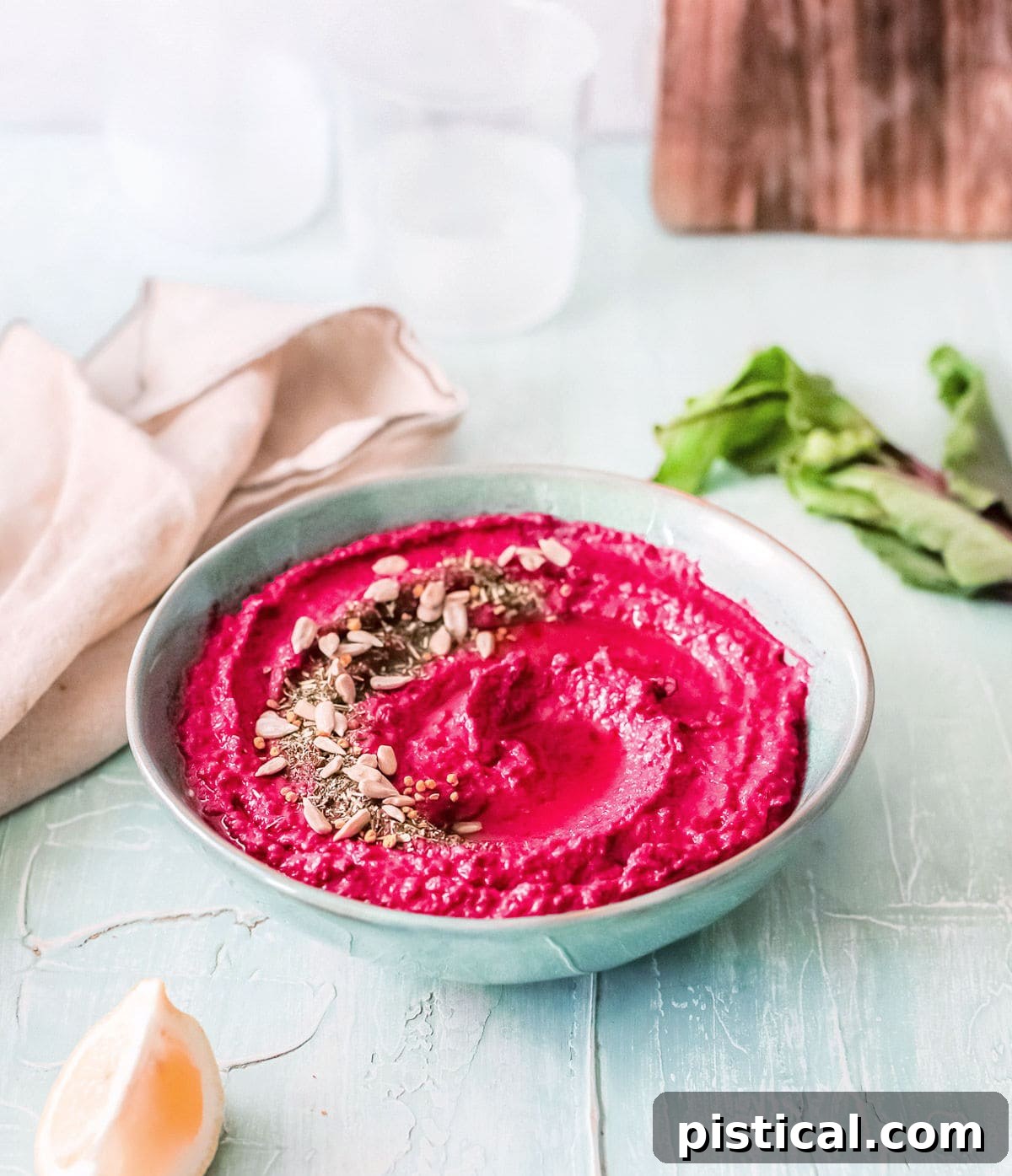 Beet Hummus: Vibrant, Versatile, Delicious 4 A beautifully textured bowl of roasted beet hummus, adorned with olive oil and seeds, resting on a rustic wooden board with a soft beige towel nearby.