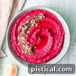Beet hummus in a light blue bowl with a beige napkin to the side.