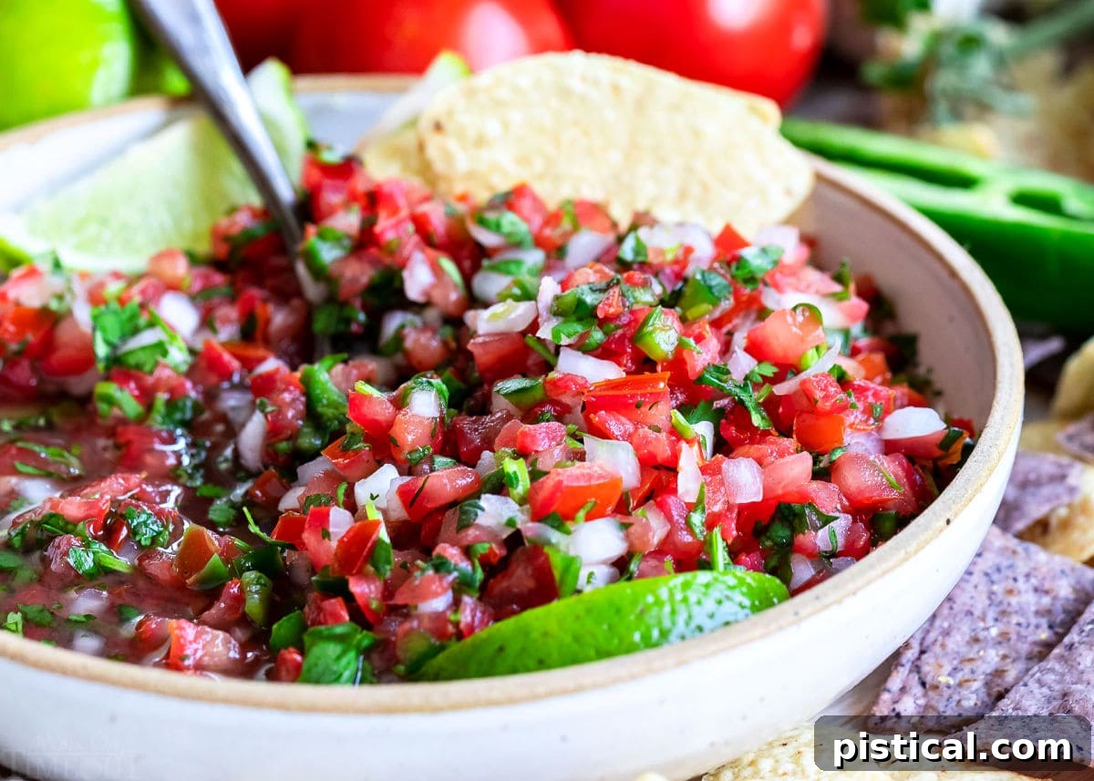 Close-up view of freshly mixed Pico de Gallo in a medium-sized clay bowl, surrounded by golden tortilla chips, emphasizing its chunky texture and vibrant colors.