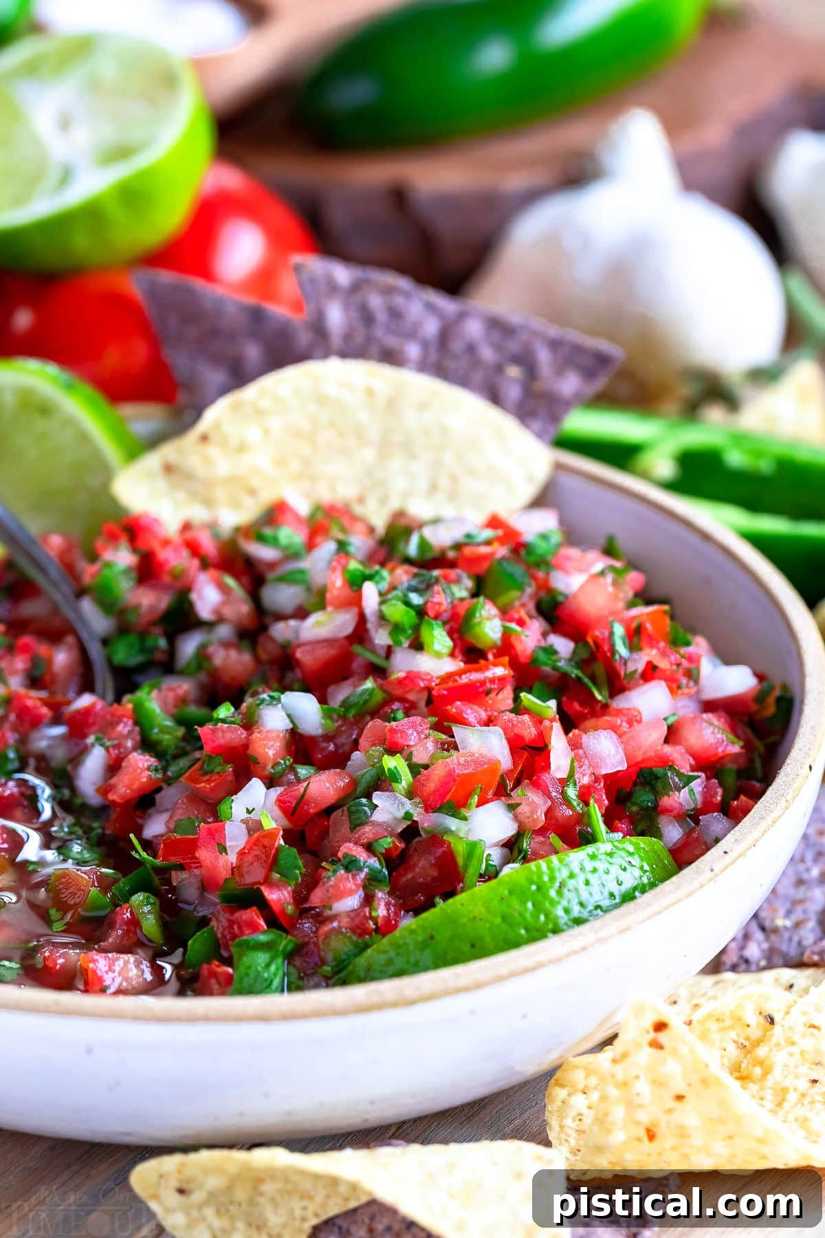 A beautifully presented bowl of salsa fresca, or Pico de Gallo, with vibrant red tomatoes, green cilantro, and white onion, accompanied by lime wedges and golden tortilla chips.