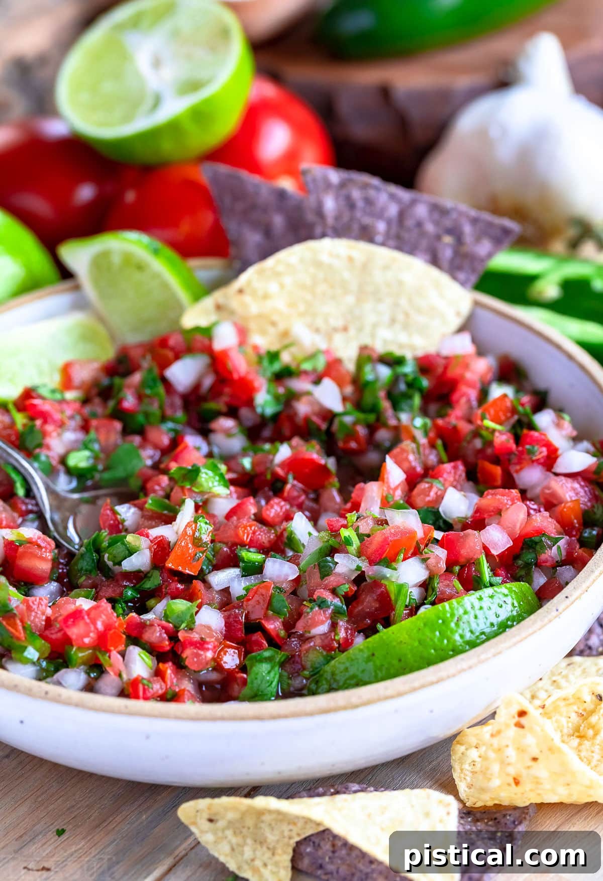 A bowl of fresh salsa fresca, or Pico de Gallo, with a portion already scooped out, revealing the vibrant ingredients. A spoon and a few tortilla chips rest in the bowl, ready for enjoyment.
