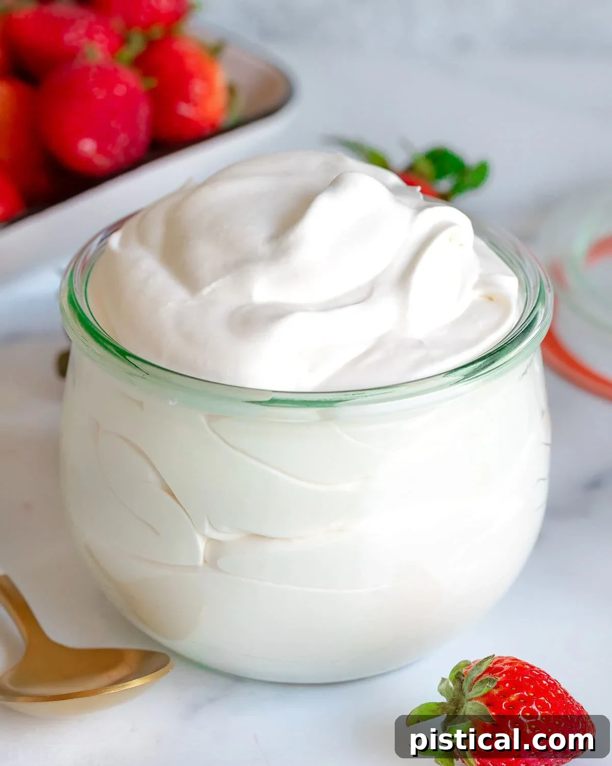 Fluffy homemade whipped cream in a large glass jar, with fresh strawberries scattered around.