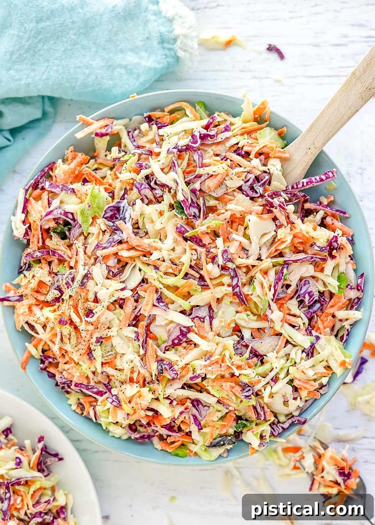 Freshly prepared coleslaw in a light blue serving bowl, with a wooden spoon resting inside, ready for a summer meal.