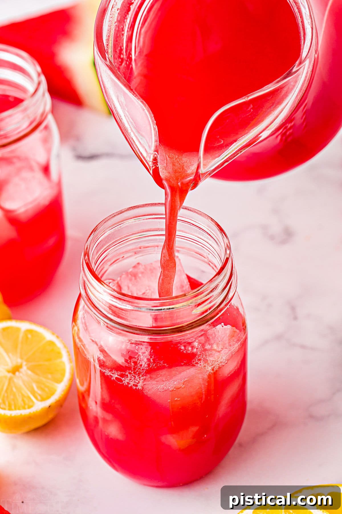 Watermelon lemonade being poured from a pitcher into a large glass filled with ice, ready to be served and enjoyed.