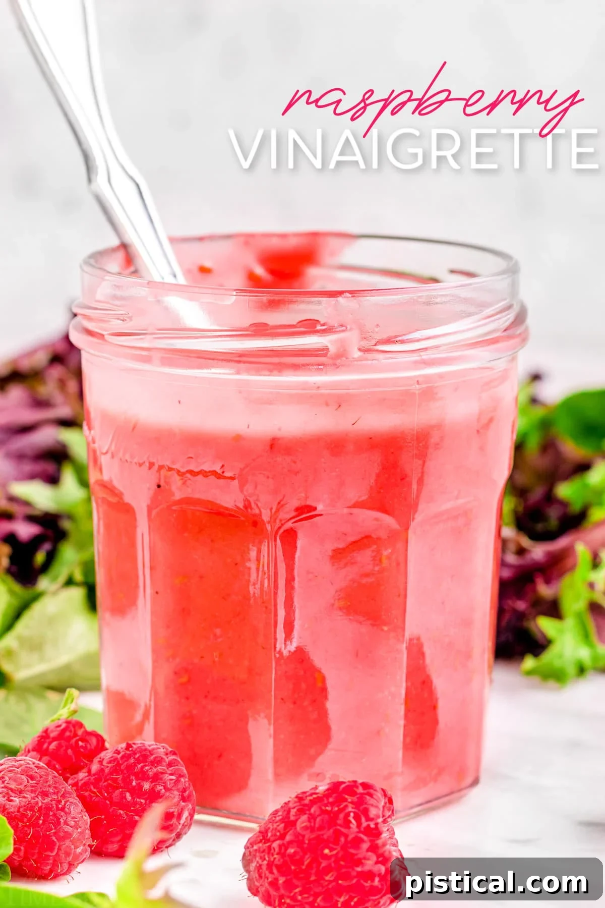 A glass jar filled with vibrant raspberry vinaigrette, with a small spoon inserted, against a blurred background of fresh ingredients. The image also contains a title overlay indicating 'Raspberry Vinaigrette'.