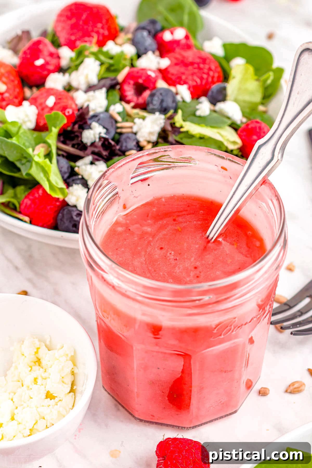 A jar of homemade raspberry dressing placed prominently in front of a fresh, colorful bowl of salad, ready to be enjoyed.