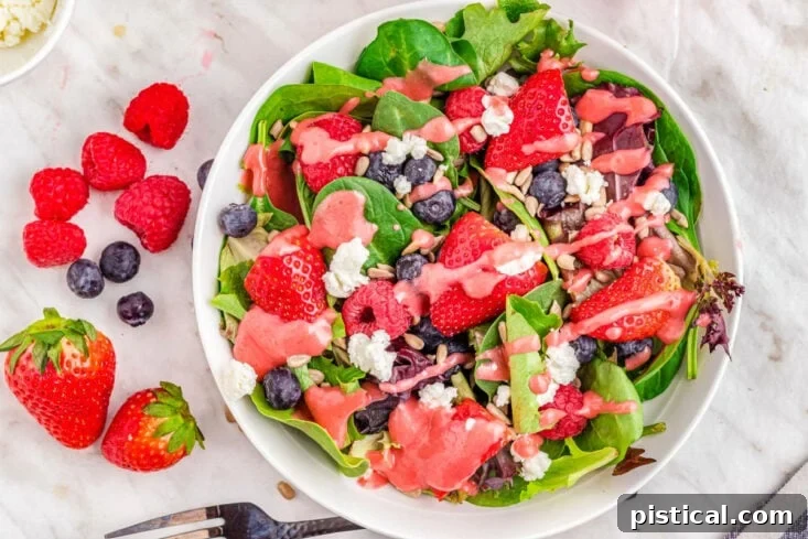Close-up, top-down view of a berry salad on a white plate, drizzled with a rich raspberry vinaigrette dressing, highlighting its fresh ingredients.