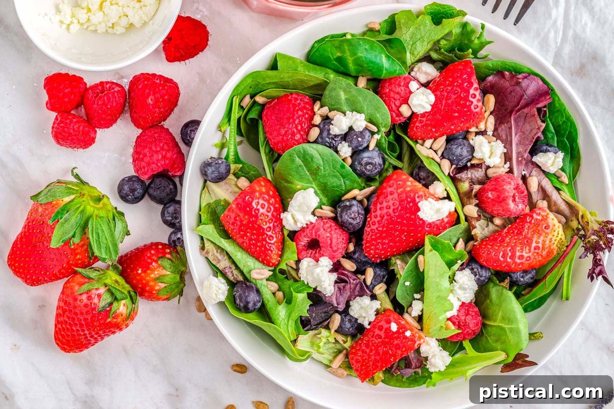 A top-down view of a colorful berry salad, elegantly presented without dressing, showcasing the freshness of the berries, spinach, goat cheese, and sunflower seeds.