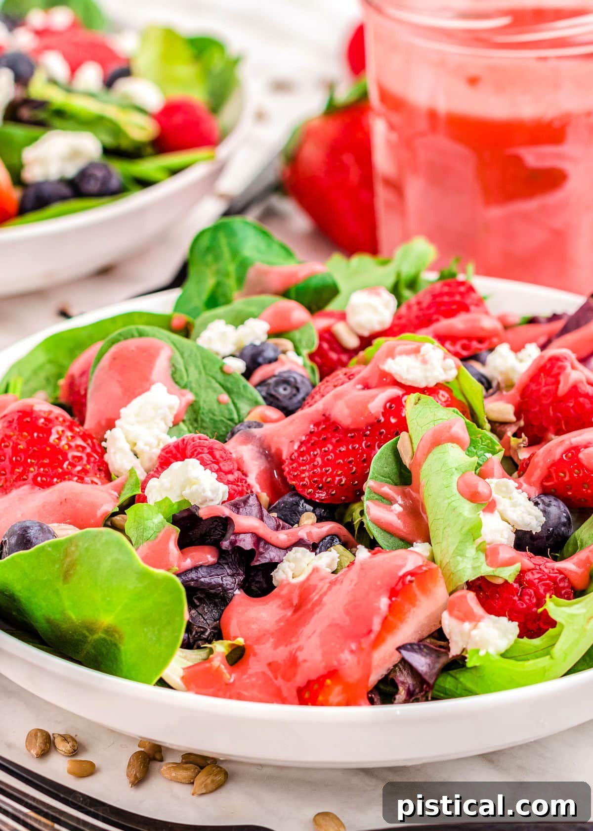 A vibrant summer berry salad with raspberry vinaigrette in a glass jar in the background, perfectly plated and ready to be enjoyed.