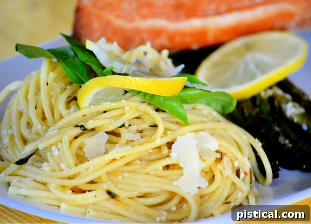 Zesty Lemon Pasta 7 lemon spaghetti on white plate with asparagus and salmon garnished with lemon and basil and Parmesan