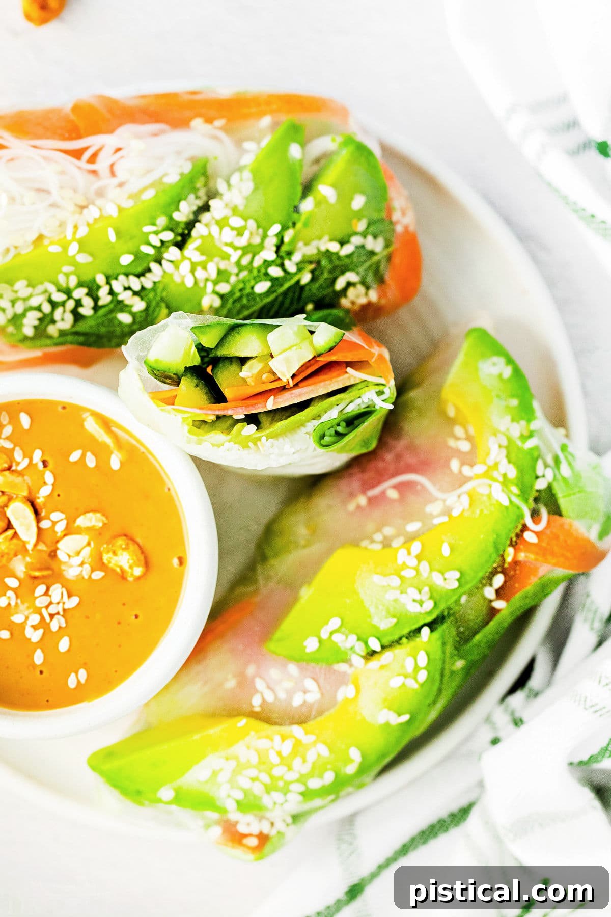 top down look at summer rolls on white plate with one cut in half. peanut dipping sauce in small bowl on the plate too.