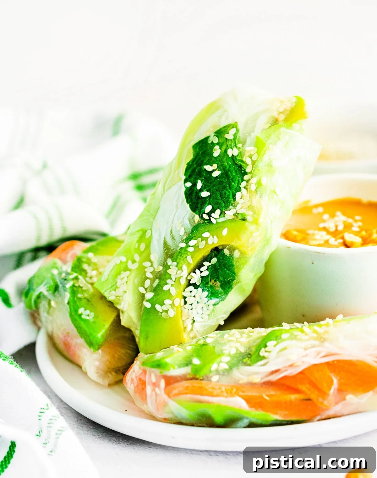 three summer rolls on white plate with peanut dipping sauce.