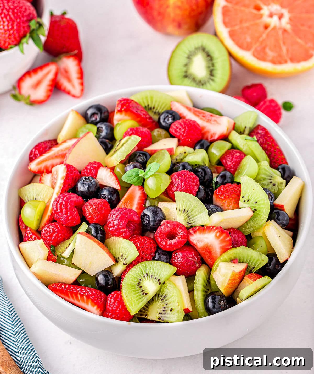 Nature's Candy Bowl 6 A beautifully vibrantly colored fruit salad in a white serving bowl, showcasing a rich mix of raspberries, kiwis, apples, blueberries, and strawberries.