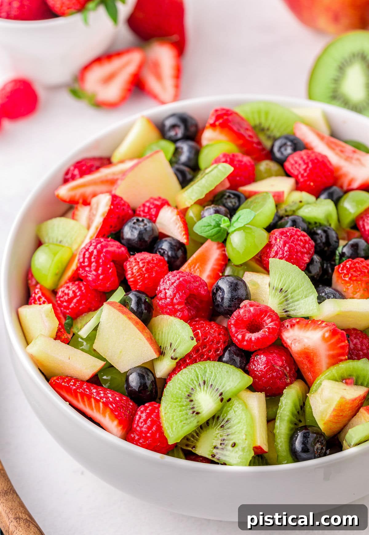 Nature's Candy Bowl 7 A close-up view of a vibrant summer fruit salad in a large white serving bowl, showcasing bright red strawberries, raspberries, green kiwis, grapes, and blueberries.
