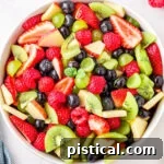 Nature's Candy Bowl 8 fruit salad in white bowl ready to serve with title overlay at top of image. fruit salad has kiwis, strawberries grapes and more.