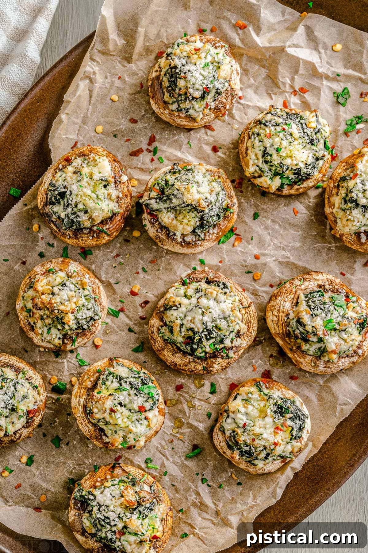 Silky Stuffed Mushrooms with Herbs and Garlic 3 tray full of stuffed mushrooms sitting on crumpled brown parchment paper and sprinkled with fresh parsley.