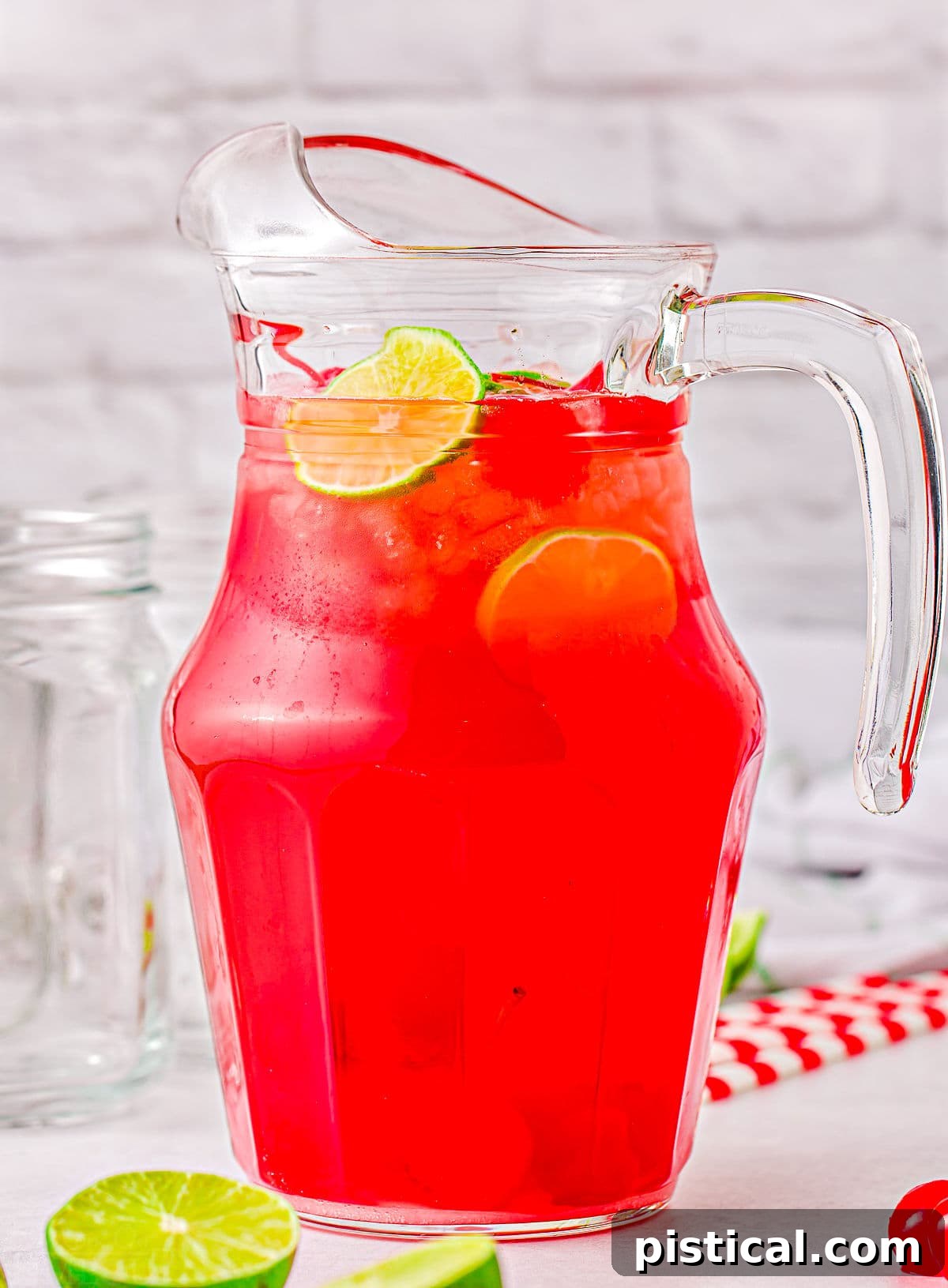 Tall glass pitcher filled with vibrant homemade cherry limeade, beautifully garnished with fresh lime slices floating both within and around the pitcher.