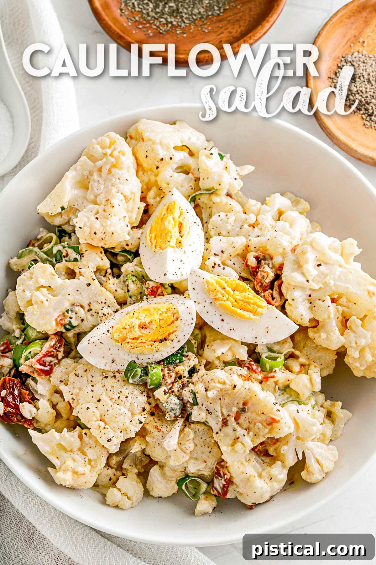 Cauliflower salad served in a white bowl, resembling potato salad, garnished with hard-boiled egg slices and fresh herbs.
