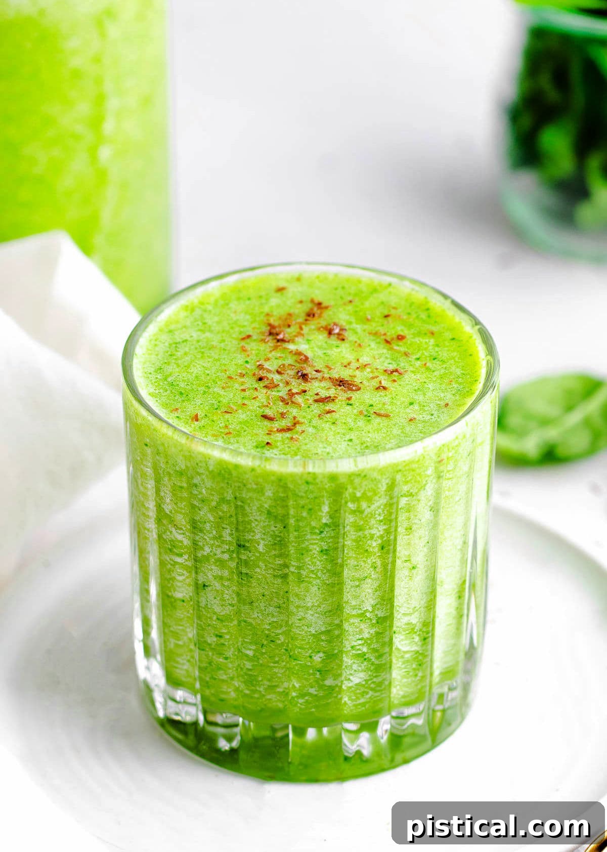 A simple green smoothie recipe in a glass, resting on a small white plate in front of a blender, ready to be enjoyed.