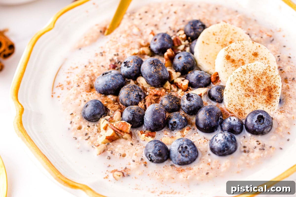 Steel cut oatmeal topped with blueberries, pecans, and cinnamon in a white bowl with a gold spoon, ready to be enjoyed.