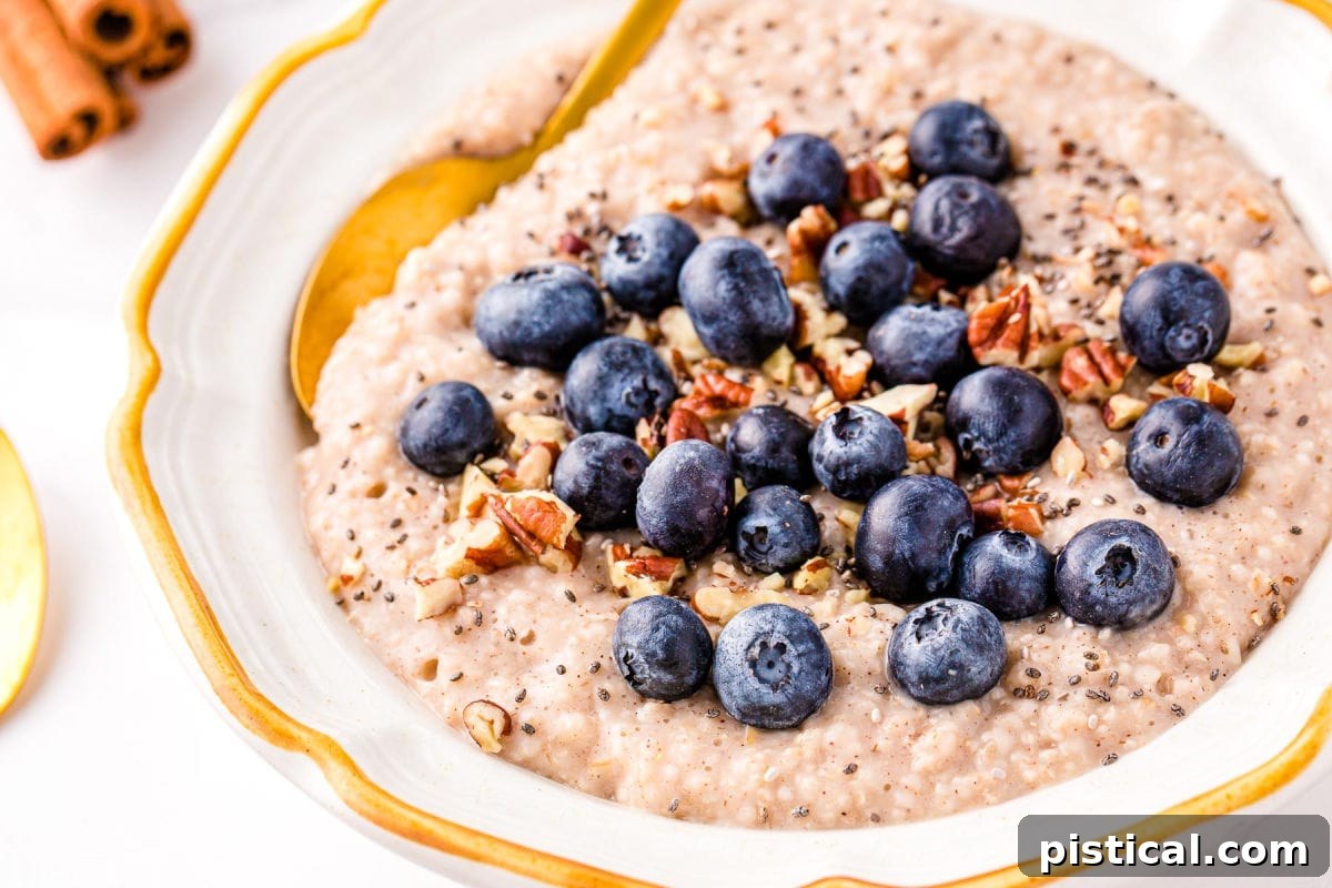 Steel cut oatmeal topped with blueberries, pecans, and cinnamon in a white bowl with a gold spoon.
