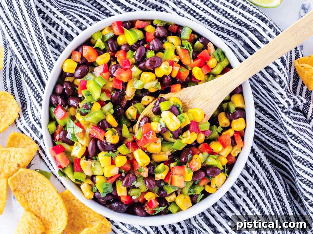 A charming white bowl filled with black bean and corn salsa, presented on a stylish black and white striped towel. A wooden serving spoon is inserted into the salsa, ready for dipping. The setting evokes a fresh, homemade feel.