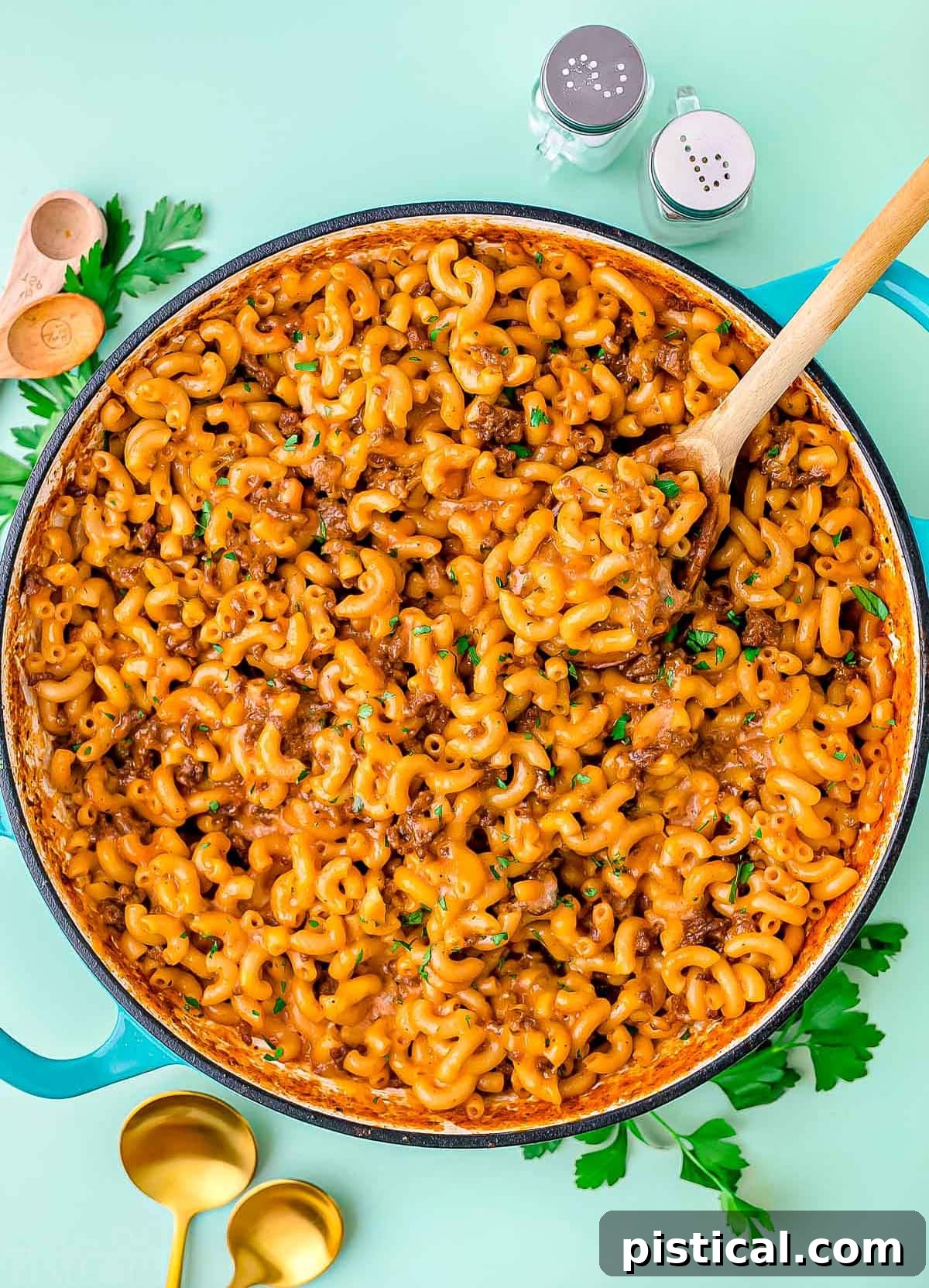 skillet of homemade hamburger helper garnished with chopped fresh parsley. background is light aqua colored.
