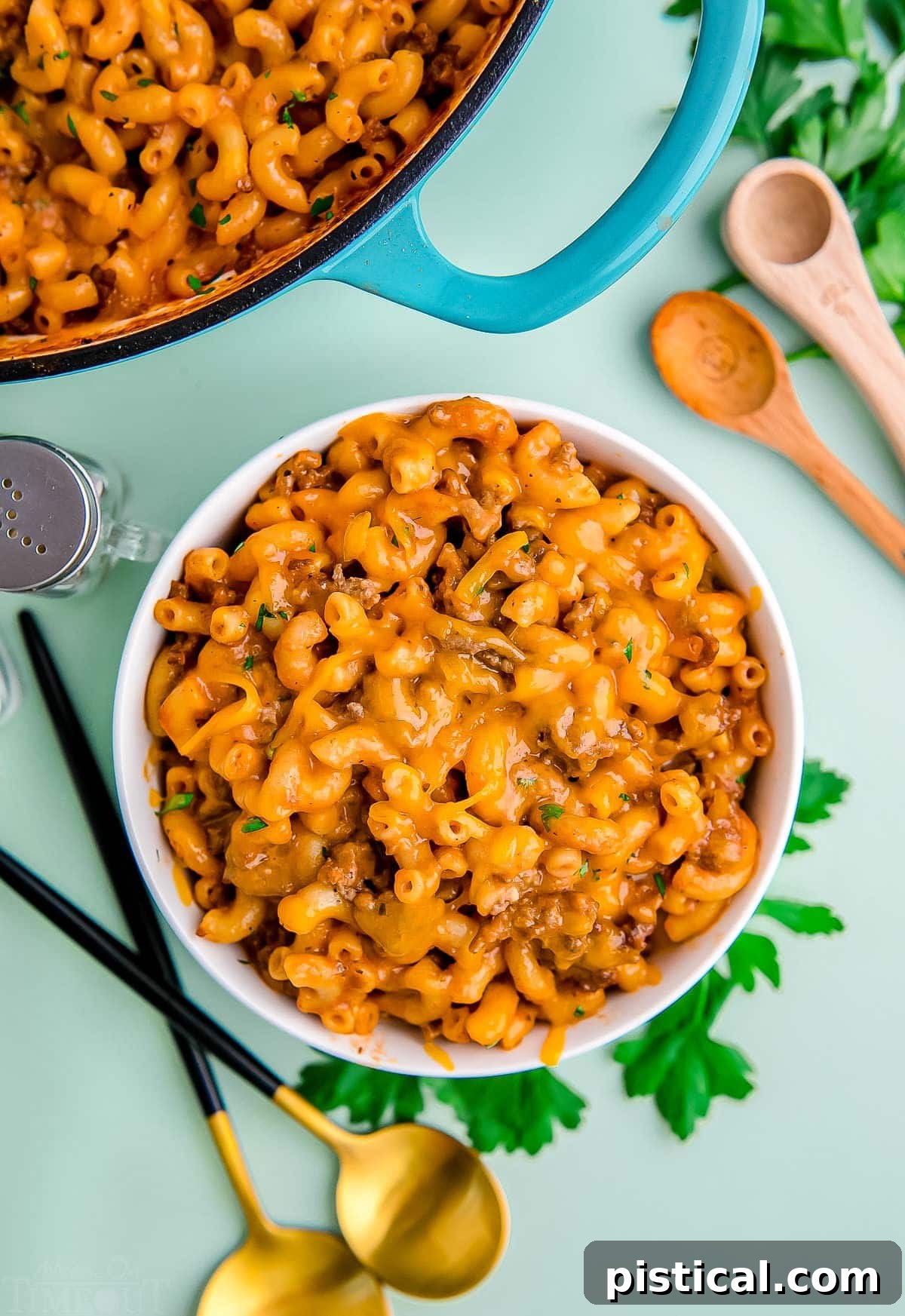 top down look at bowl of hamburger helper sitting next to skillet with the rest of it. light green background. 