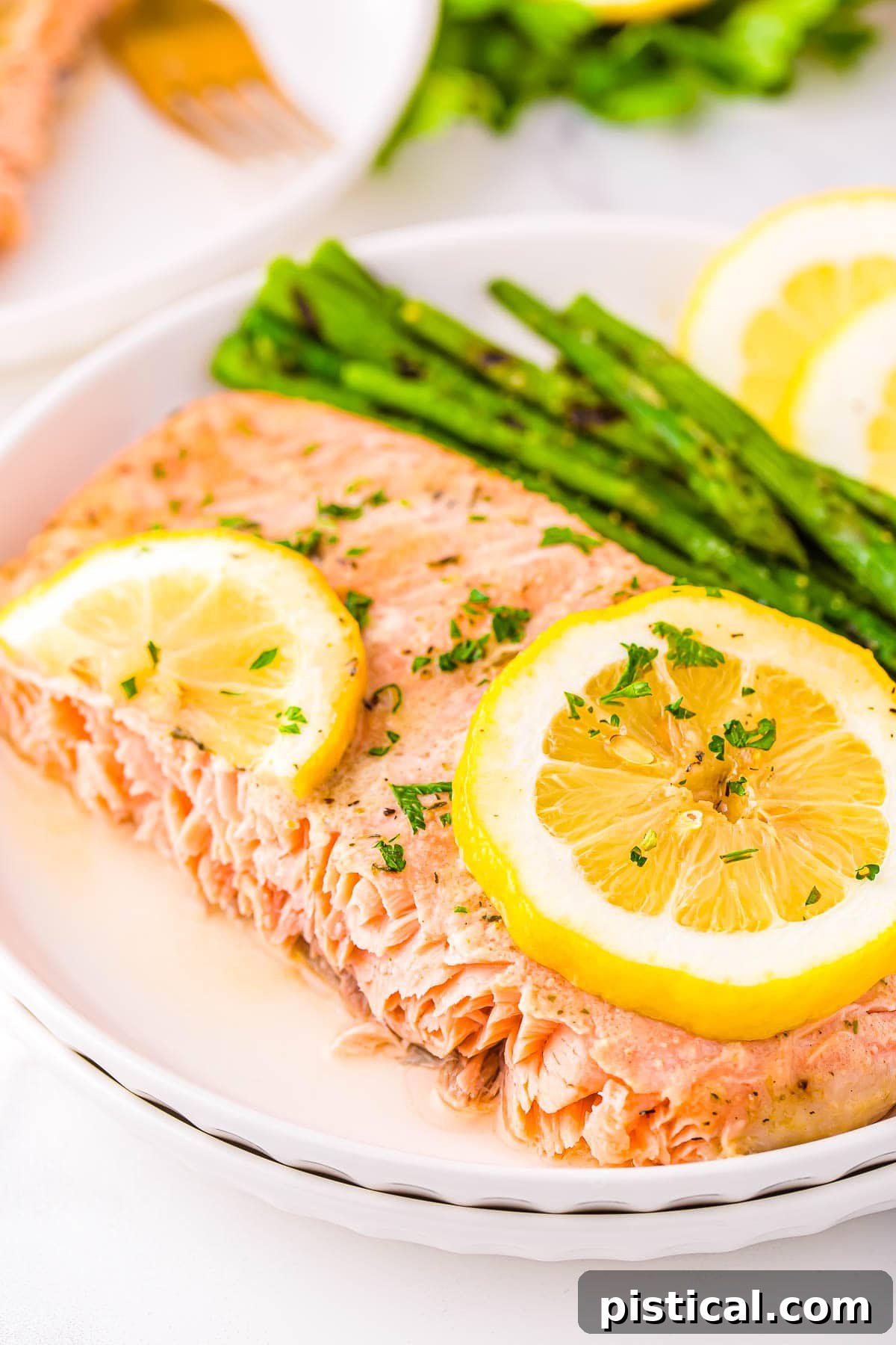 piece of baked salmon plated with asparagus and fresh lemon slices sitting on white plate.