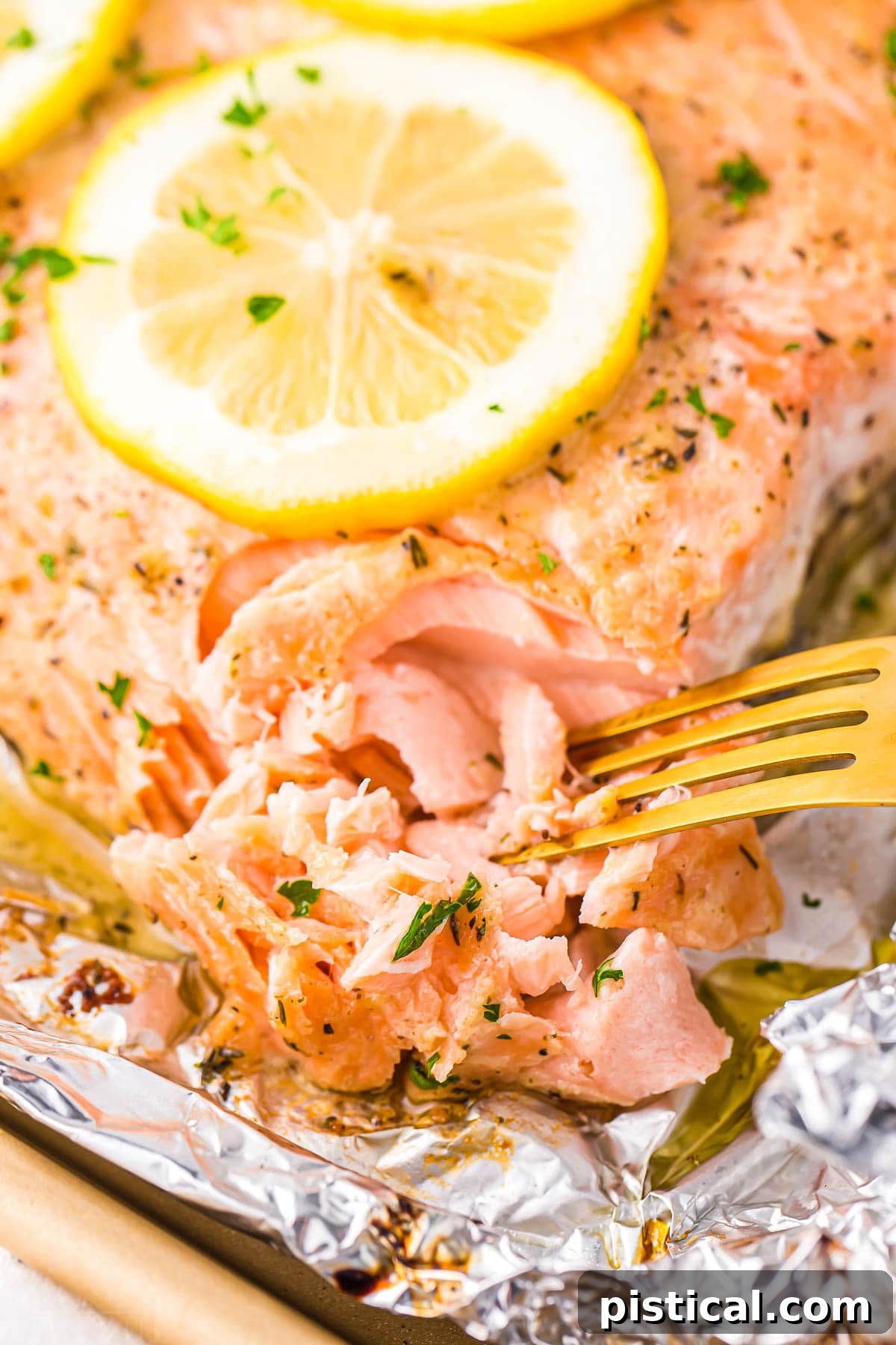 tender flaky salmon being flaked with a gold fork on a large salmon filet topped with a lemon slice.