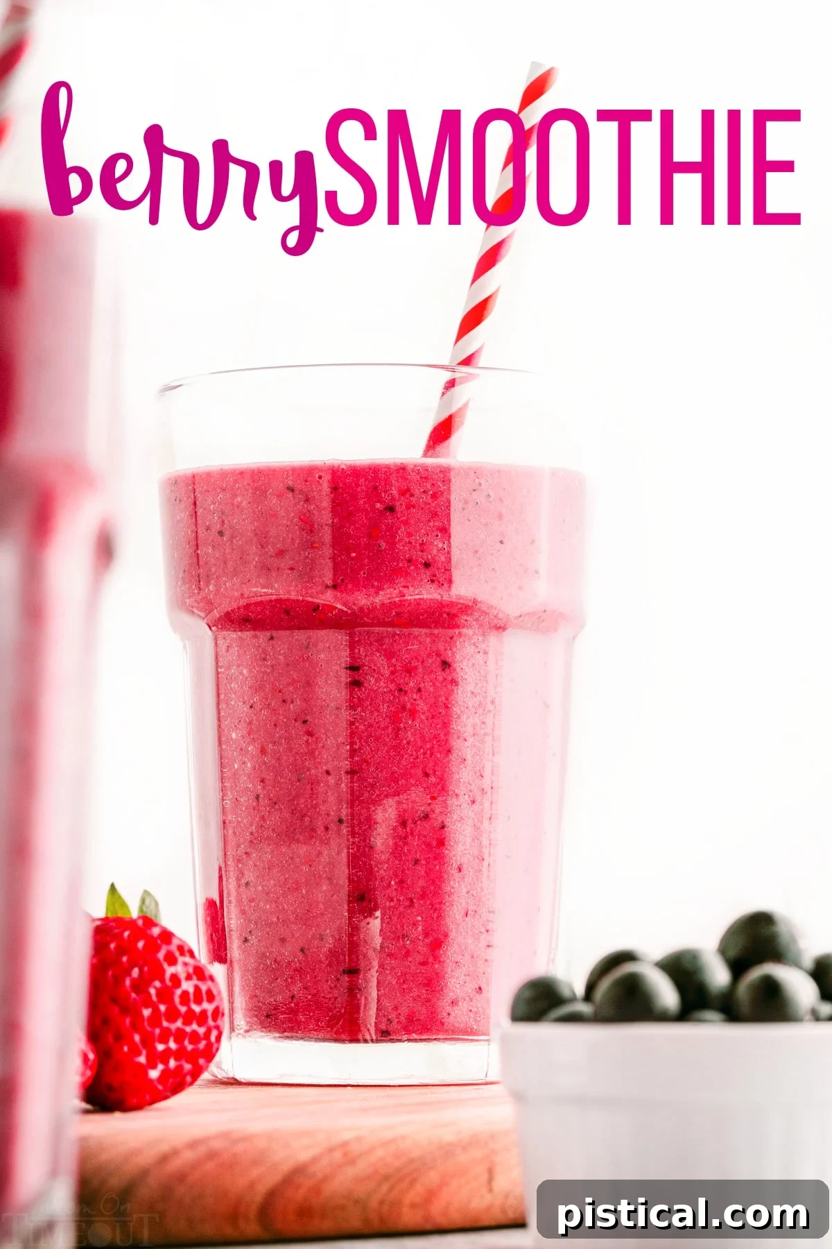 berry smoothie in tall glass with striped paper straw sitting on wood cutting board next to a small bowl of blueberries. title overlay at top of image.