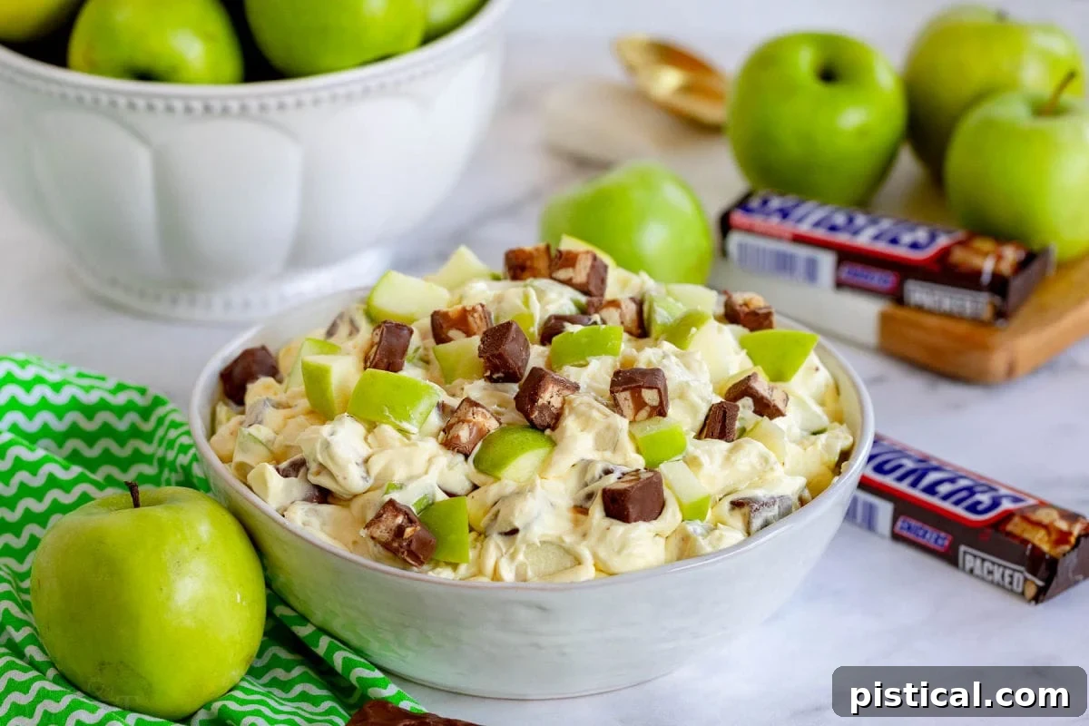apple salad with snickers mixed in in large white bowl.