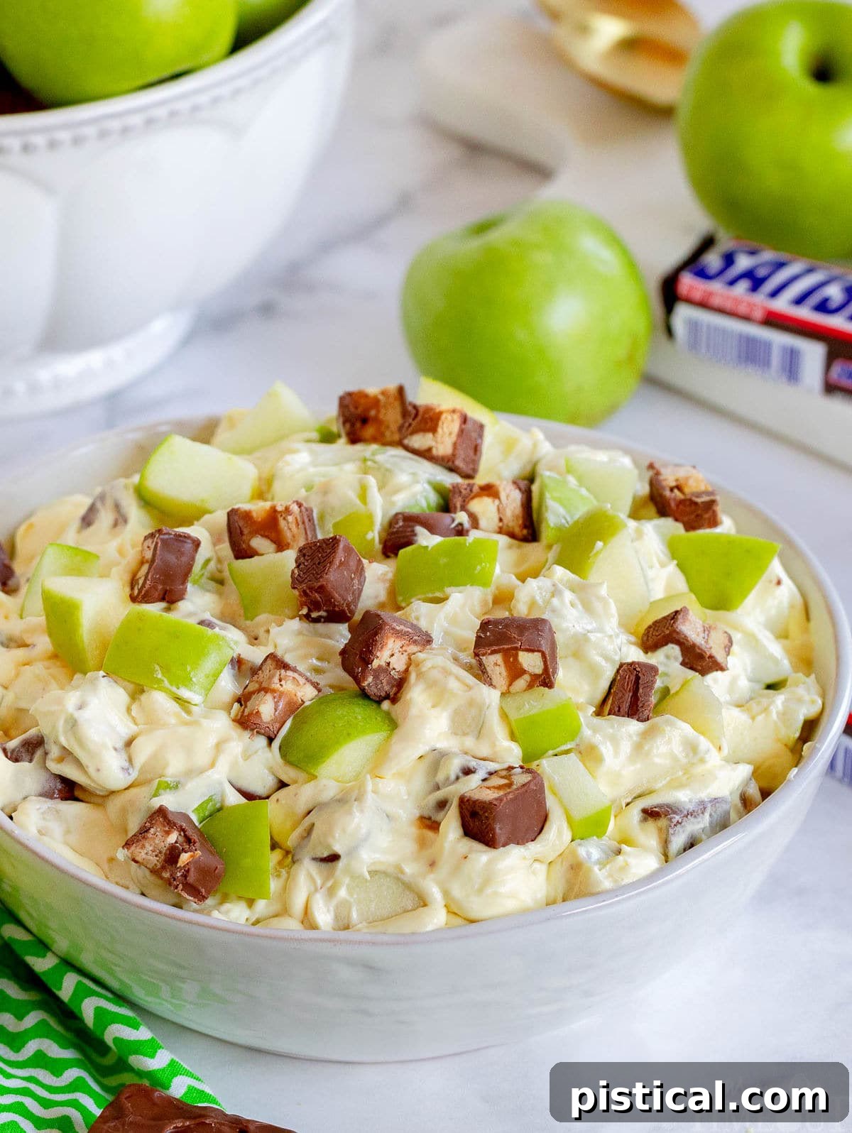apple salad with snickers mixed in in large white bowl.