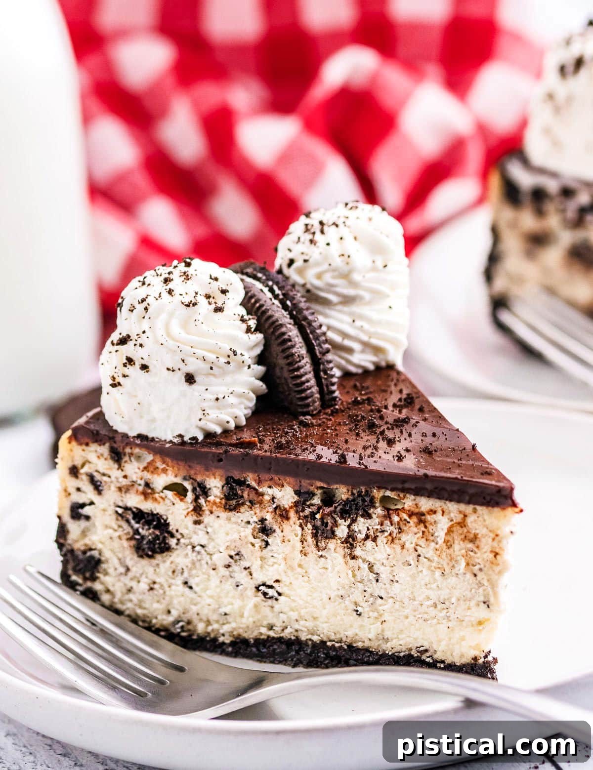 A perfectly portioned slice of Oreo cheesecake rests on a pristine white plate, with a rustic red checkered napkin softly blurred in the background, highlighting the dessert's elegance.