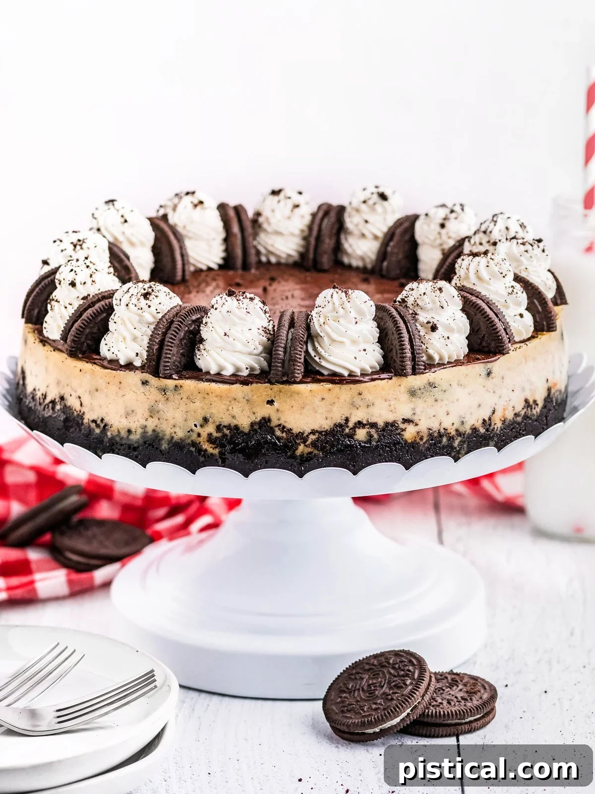 A stunning whole Oreo cheesecake displayed on a elegant white metal cake stand, beautifully topped with generous swirls of whipped cream and whole Oreo cookies as garnish.